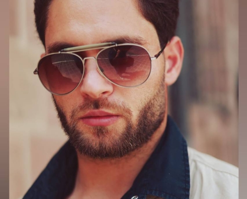 Es klingt, als würden Sie ein Bild von "Callboy Matteo" beschreiben. Wenn Sie eine schriftliche Beschreibung benötigen, die sich für den Alt-Text eignet, finden Sie hier eine knappe Version: "Ein Mann mit kurzen dunklen Haaren und einem Bart, der eine Piloten-Sonnenbrille und eine beigefarbene Jacke mit dunklem Kragen trägt, blickt selbstbewusst in die Kamera. Der unscharfe Hintergrund deutet auf einen Außenbereich hin." Lassen Sie mich wissen, wenn Sie diese Beschreibung erweitern möchten oder Informationen in einem anderen Format benötigen!.