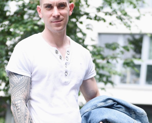 Es klingt, als ob Sie eine beschreibende Zusammenfassung eines Bildes mit dem Titel "Callboy Dennis" wünschen. Hier ist eine verfeinerte Beschreibung, die auf den von Ihnen angegebenen Details basiert: --- Beschreibung: Callboy Dennis steht selbstbewusst im Freien, sein kurzes Haar ist ordentlich gestylt. Sein linker Arm, der mit Tattoos verziert ist, ist deutlich sichtbar, während er lässig eine Jeansjacke in einer Hand hält. Er trägt ein knackiges weißes T-Shirt mit Knöpfen, das einen Kontrast zu seiner eingefärbten Haut bildet. Hinter ihm bilden üppige grüne Bäume und die weichen Umrisse eines verschwommenen Gebäudes eine entspannte städtische Kulisse. --- Wenn Sie dieses Bild für etwas Bestimmtes benötigen (z. B. Alt-Text für Barrierefreiheit, Social-Media-Post), lassen Sie es mich wissen, damit ich es anpassen kann!.
