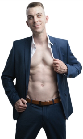 Dennis posiert selbstbewusst in einem blauen Anzug, Jacke und Hemd offen, um seinen durchtrainierten Oberkörper zu zeigen, und lächelt in die Kamera vor einem weißen Hintergrund.