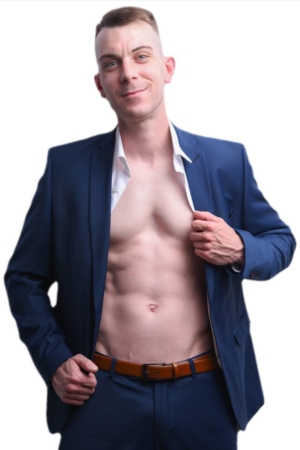 Dennis, in einem blauen Anzug ohne Hemd, zeigt seine straffe Brust und seine Bauchmuskeln und lächelt selbstbewusst in die Kamera vor einem weißen Hintergrund.