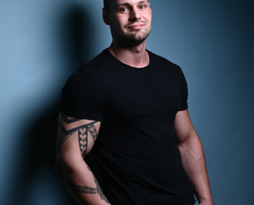 Diese Beschreibung vermittelt das Bild einer Person mit lässiger und entspannter Haltung. Die kurzen Haare und das Tattoo verleihen ihr einen persönlichen Stil, während das schwarze T-Shirt und die blauen Jeans einen klassischen, entspannten Look suggerieren. Das leichte Lächeln deutet auf ein freundliches oder zugängliches Auftreten hin. Wenn Sie spezielle Fragen haben oder weitere Einzelheiten zu dieser Person benötigen, können Sie diese gerne stellen!.