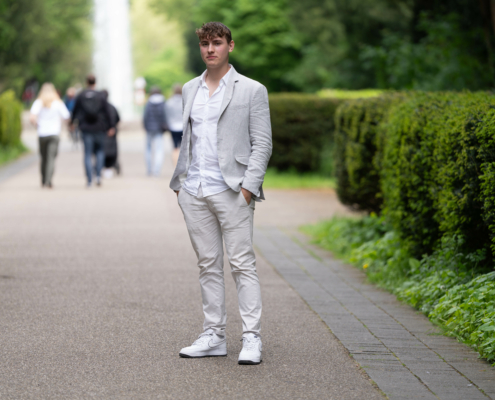Die Szene, die Sie beschreiben, klingt ziemlich friedlich und stilvoll. Die Wahl des Mannes für einen hellgrauen Anzug und weiße Turnschuhe verleiht der traditionellen Abendgarderobe eine moderne und lässige Note und passt gut in die entspannte Atmosphäre des Parks. Der von grünen Hecken gesäumte Weg verleiht der Umgebung Struktur, während die Bäume im Hintergrund eine üppige, natürliche Kulisse bilden. Die Anwesenheit anderer Spaziergänger lässt darauf schließen, dass es sich um einen lebendigen öffentlichen Raum handelt, in dem man die Natur genießen und vielleicht an geselligen Aktivitäten oder gemütlichen Spaziergängen teilnehmen kann. Die Kombination aus Mode und Natur in dieser Umgebung schafft eine harmonische Mischung aus urbanem Stil und Schönheit im Freien.