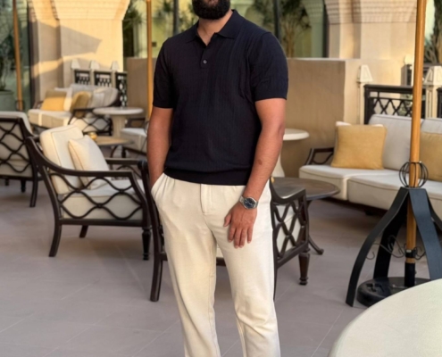 Es klingt, als würden Sie ein Bild beschreiben, auf dem ein Mann namens Callboy Kaan selbstbewusst auf einer Terrasse steht. Er wird als dunkelhaarig und bärtig beschrieben und ist leger mit einem schwarzen Poloshirt, einer hellen Hose und weißen Turnschuhen bekleidet. Er posiert mit den Händen in den Taschen und lächelt in die Kamera. Die Umgebung besteht aus einem beigen Fliesenboden, Tischen und Stühlen im Freien und Sonnenschirmen, die Schatten spenden. Wenn Sie weitere Analysen oder Hilfe bei dieser Beschreibung benötigen - z. B. um sie weiter zusammenzufassen oder für soziale Medien oder andere Kontexte zu verwenden - lassen Sie es mich bitte wissen!.