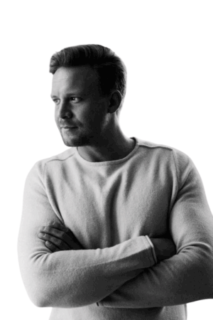 Ein Schwarz-Weiß-Foto, das Callboy Michael, einen Mann mit kurzen Haaren, zeigt. Er ist mit einem hellen Pullover bekleidet und steht mit verschränkten Armen da. Sein Blick ist nachdenklich, während er nach rechts blickt. Der Hintergrund ist schlicht und weiß und lenkt die Aufmerksamkeit auf Michaels nachdenkliche Pose. Wenn Sie ein aktuelles Foto benötigen, lassen Sie mich wissen, welche Tools oder Dienste Sie verwenden - ich kann Ihnen dabei helfen, die Aufforderung zur Erstellung eines Fotos anzupassen!.