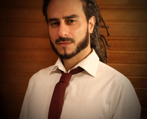 Es klingt, als würdest du eine bezaubernde und charismatische Person mit einem unverwechselbaren Stil beschreiben. Die Kombination aus langen Dreadlocks, kurzem Bart und formeller Kleidung kreiert einen einzigartigen Look, der Selbstvertrauen und Charme ausstrahlt. Die gedämpfte Beleuchtung vor einer Holzwand verleiht der Szene Wärme und unterstreicht sein zugängliches und dennoch selbstbewusstes Auftreten. Diese Beschreibung weckt tatsächlich den Charme, der oft mit Callboy Aslan in Verbindung gebracht wird – eine Mischung aus lässigem Stil und Eleganz, die mühelos Aufmerksamkeit erregt.