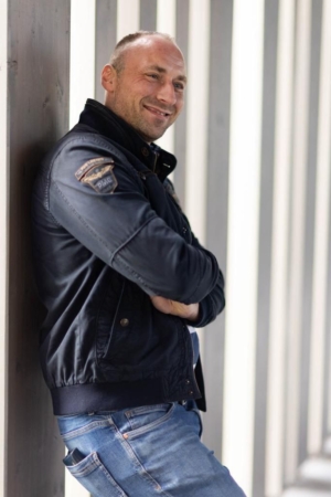 Auf jeden Fall! Hier ist ein beschreibender Absatz für deine Szene: Callboy Matteo, gekleidet in eine elegante dunkle Jacke und enge Bluejeans, lehnt lässig an der Wand. Seine Arme sind selbstbewusst verschränkt, und ein charmantes Lächeln umspielt seine Lippen. Hinter ihm werfen hohe vertikale Säulen rhythmische Schatten und erzeugen ein auffälliges geometrisches Muster, das die Szene mit urbaner Eleganz umrahmt. Wenn du möchtest, dass dieser Prompt in einen Bildgenerierungs-Prompt umgewandelt wird (für Tools wie Midjourney oder DALL-E), lass es mich wissen!.