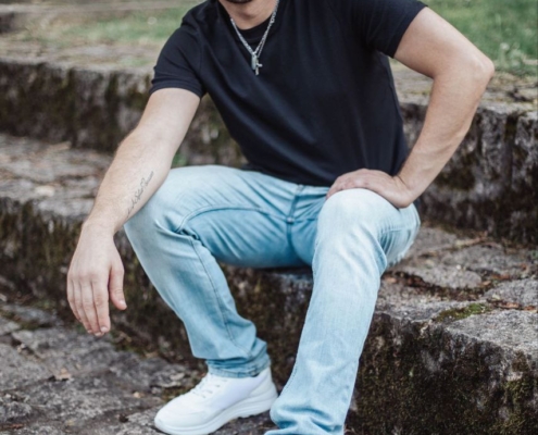 Natürlich! Hier ist eine überarbeitete Version Ihrer Beschreibung, um sie verständlicher oder kreativer zu gestalten: Ein Mann mit kurzen Haaren und Bart, bekleidet mit schwarzem T-Shirt, hellblauen Jeans und weißen Turnschuhen, sitzt auf einer Steintreppe im Freien. Üppiges Grün umgibt ihn, während Callboy Matteo mit ernster Miene aufmerksam in die Kamera blickt. Wenn Sie weitere Anpassungen wünschen (z. B. Text, Bildunterschriften, Einleitung usw.), lassen Sie es mich wissen!.