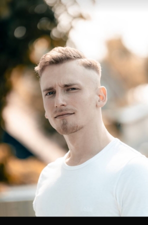 Es klingt, als würden Sie ein Bild von einem jungen Mann namens Gabriel L. beschreiben, der als Callboy arbeitet. Er hat kurze, hellbraune Haare und einen gestutzten Bart, trägt ein weißes T-Shirt und blickt mit neutralem Gesichtsausdruck in die Kamera. Das Foto wurde im Freien mit einem unscharfen Hintergrund aufgenommen, der sein ruhiges Auftreten hervorhebt. Wenn Sie Hilfe beim Verfassen einer Profilbeschreibung oder der Bildunterschrift benötigen oder weitere Informationen zur Darstellung von Charaktereigenschaften in solchen Bildern benötigen, lassen Sie mich bitte wissen, wie ich Ihnen helfen kann!.