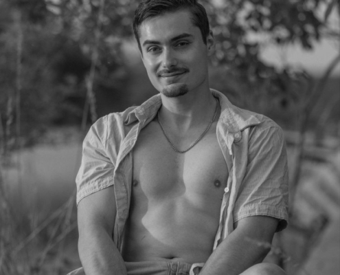 Es klingt, als würden Sie ein Foto mit einer ruhigen, natürlichen Ausstrahlung beschreiben. Der junge Mann in legerer Kleidung - aufgeknöpftes Hemd und Shorts - sitzt bequem auf einem Steinsockel im Freien. Seine kurzen Haare und sein leichtes Lächeln tragen zu einer offenen, entspannten Stimmung bei. Der Hintergrund aus Bäumen und Natur verleiht der Szenerie eine organische Atmosphäre. Die Wiedergabe dieses Bildes in Schwarz-Weiß verstärkt die Zeitlosigkeit und den Kontrast und betont die Texturen - den Steinsims, den Stoff seiner Kleidung, seine Haut - und hebt gleichzeitig Licht und Schatten in der Umgebung hervor. Wenn Sie weitere Beschreibungen benötigen oder dieses Bild als Inspiration für einen Text oder ein Bild verwenden möchten, lassen Sie mich wissen, wie ich Ihnen helfen kann!.