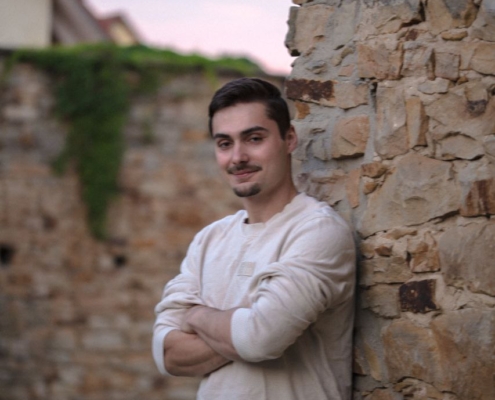 Es klingt, als würden Sie ein Foto oder Bild eines jungen Mannes beschreiben, der in einer natürlichen, entspannten Umgebung posiert. Die Szene fängt das goldene Licht des Sonnenuntergangs ein und hebt seine Gesichtszüge hervor - kurzes dunkles Haar, Schnurrbart, ruhiges Auftreten. Er steht mit verschränkten Armen an eine Steinmauer gelehnt und trägt ein helles, langärmeliges Hemd und Jeans. Wenn Sie bei dieser Beschreibung Hilfe benötigen (z. B. bei der Umsetzung in eine künstlerische Vorlage, beim Schreiben einer Geschichte oder bei der Suche nach Details für die Bilderstellung), lassen Sie es mich bitte wissen!.