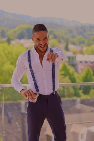 Es klingt, als würden Sie das Bild eines Mannes namens "Callboy Steve" beschreiben, der mit einem weißen Hemd, blauen Hosenträgern und einer dunklen Hose gut gekleidet ist. Er steht auf einem Balkon, lächelt selbstbewusst und deutet in die Kamera, während er einen Stapel Bargeld in der Hand hält. Der Hintergrund ist unscharf, zeigt aber grüne Bäume und einige Gebäude. Wenn Sie Hilfe beim Schreiben einer Bildunterschrift oder eines Alt-Textes für die Barrierefreiheit benötigen, finden Sie hier ein Beispiel: Alt-Text: Ein Mann, bekannt als Callboy Steve, steht auf einem Balkon und trägt ein weißes Hemd, blaue Hosenträger und eine dunkle Hose. Er lächelt breit, während er mit einer Hand in die Kamera zeigt und in der anderen einen aufgefächerten Stapel Bargeld hält. Im unscharfen Hintergrund sind grüne Bäume und mehrere Gebäude zu sehen. Lassen Sie mich wissen, wenn Sie diese Beschreibung verfeinern möchten oder sie für einen anderen Zweck benötigen!.