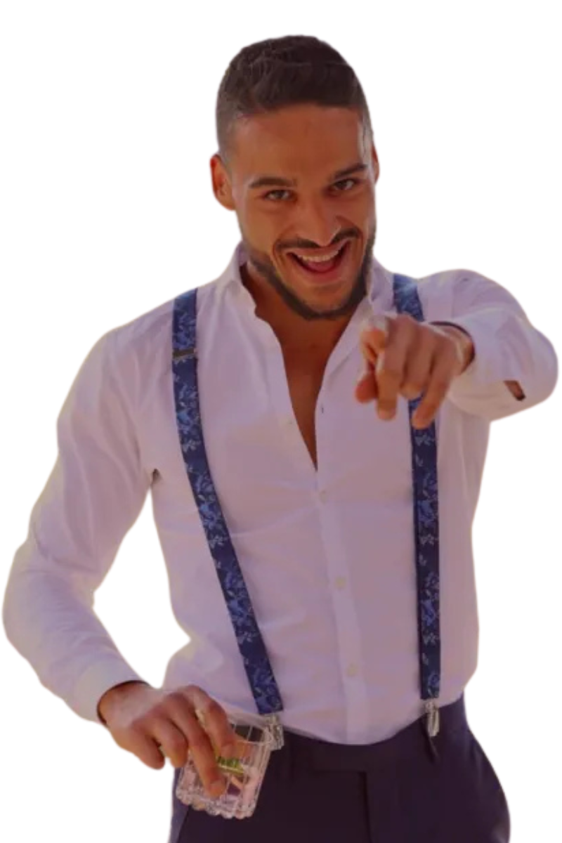 Ein Mann, der an den Callboy Alex Léon erinnert, steht lächelnd da und strahlt eine verspielte und fröhliche Ausstrahlung aus. Er trägt ein frisches weißes Hemd mit blauen Hosenträgern, was seinem Aussehen einen Hauch von flottem Stil verleiht. Mit seiner rechten Hand zeigt er direkt in die Kamera und bindet den Betrachter freundlich ein. In der linken Hand hält er einen kleinen durchsichtigen Behälter - vielleicht für Süßigkeiten oder einen anderen kleinen Gegenstand -, der der Szene einen Hauch von Neugierde verleiht. Sein gesamter Gesichtsausdruck ist fröhlich und unbeschwert, was die lustige Atmosphäre des Moments unterstreicht.