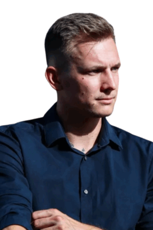 Der Callboy Matthias steht vor einem strahlend weißen Hintergrund. Er hat kurzes, hellbraunes Haar und trägt ein dunkles, marineblaues Hemd. Sein Blick ist zur Seite gerichtet, sein Gesichtsausdruck ernst und nachdenklich, was ihm eine ruhige, intensive Ausstrahlung verleiht. Wenn Sie dies in ein Bild verwandelt haben möchten oder weitere Details zur Visualisierung benötigen, lassen Sie es mich bitte wissen!.