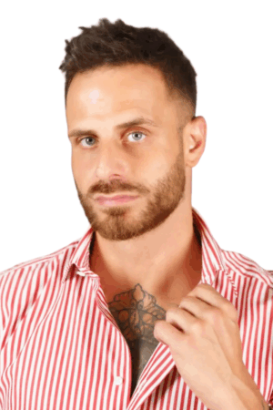 Callboy Bruno steht mit dem Gesicht nach vorne, sein kurzes braunes Haar ist ordentlich frisiert und ein Bart betont sein Kinn. Er trägt ein rot-weiß gestreiftes Hemd, dessen Kragen leicht geöffnet ist und einen Blick auf eine komplizierte Brusttätowierung darunter freigibt - ein Detail, das auf unerzählte Geschichten hinweist. Sein Gesichtsausdruck ist ruhig und neutral, seine Augen begegnen dem Blick des Betrachters ohne erkennbare Emotionen. Vor dem sauberen weißen Hintergrund sind Brunos Gesichtszüge und Kleidung klar und unverwechselbar; die Streifen seines Hemdes ziehen die Aufmerksamkeit auf sich, während der offene Kragen auf subtile Weise eine weitere Ebene seiner Persönlichkeit offenbart.