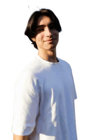 Eine junge Person mit mittellangem dunklem Haar steht vor einem weißen Hintergrund und trägt ein einfaches weißes T-Shirt. Ihr Ausdruck ist subtil charmant, mit einem leichten Lächeln, das eine zugängliche und doch selbstbewusste Ausstrahlung vermittelt - und an die unaufdringliche Ausstrahlung von Bi Callboy Luka erinnert. Die schlichte Umgebung und das Outfit betonen ihre natürliche Präsenz und die sanfte Ausstrahlung in ihren Augen, wodurch ein einladendes und authentisches Porträt entsteht.