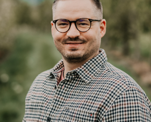Es klingt, als würden Sie ein Foto beschreiben oder eine Bildunterschrift benötigen. Hier ist eine passende Bildunterschrift oder Beschreibung auf der Grundlage Ihrer Angaben: --- Ein Mann mit kurzen braunen Haaren, Brille und ordentlich gestutztem Bart lächelt freundlich, während er im Freien steht. Er ist als Callboy Sören bekannt und trägt ein lässiges, kariertes Hemd mit Knopfleiste. Der Hintergrund zeigt sanft verschwommenes Grün unter einem bedeckten Himmel, was der Szene eine natürliche und entspannte Atmosphäre verleiht. --- Wenn Sie dies in einem anderen Stil umgeschrieben haben möchten (zum Beispiel formeller oder für soziale Medien), lassen Sie es mich wissen!.