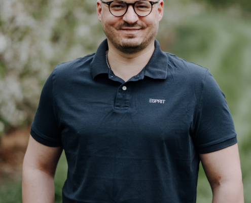 Es hört sich an, als würden Sie ein angenehmes und freundliches Porträt im Freien beschreiben, vielleicht stellen Sie sich vor, wie "Callboy Sören" seine Freizeit genießt. Wenn Sie Hilfe brauchen, um diese Bildbeschreibung zu verfeinern und sie für Erzählungen oder soziale Medien detaillierter zu gestalten, finden Sie hier eine verbesserte Version: *Ein Mann mit kurzen Haaren, einer Brille und einem marineblauen Polohemd steht auf einem grasbewachsenen Weg, der von üppigem Grün umgeben ist. Das Sonnenlicht fällt durch die Bäume im unscharfen Hintergrund, während er freundlich in die Kamera lächelt - vielleicht ist das Callboy Sören, der eine Pause einlegt und einen friedlichen Tag im Freien genießt.* Wenn Sie weitere Anpassungen wünschen oder eine andere Anfrage zu diesem Bild oder der Charakterbeschreibung haben, lassen Sie es mich einfach wissen!.
