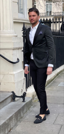Sie beschreiben eine modische Stadtszene: Ein Mann, elegant gekleidet in schwarzer Anzugsjacke und -hose mit weißem Hemd und schwarzen Halbschuhen, geht einen städtischen Bürgersteig entlang. Die Kulisse ist ein elegantes weißes Gebäude mit einem schmiedeeisernen Geländer. Der Kontrast zwischen seiner klaren, formellen Kleidung und den klassischen architektonischen Details deutet auf Raffinesse hin - vielleicht in einem eleganten Viertel oder Geschäftsviertel. Wenn Sie eine weitere Beschreibung oder Analyse benötigen oder dieses Bild für kreative Texte oder andere Zwecke visualisieren möchten, lassen Sie es mich wissen!.