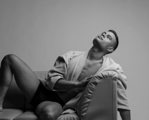 Ein Mann, wie Callboy Bruno, liegt in Unterwäsche und offenem Bademantel auf einer Couch und blickt nach oben. Schwarz und weiß; dramatische Beleuchtung.